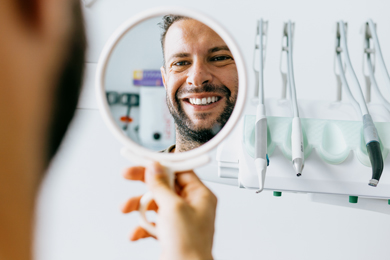 male patient smiling into mirror at dentists